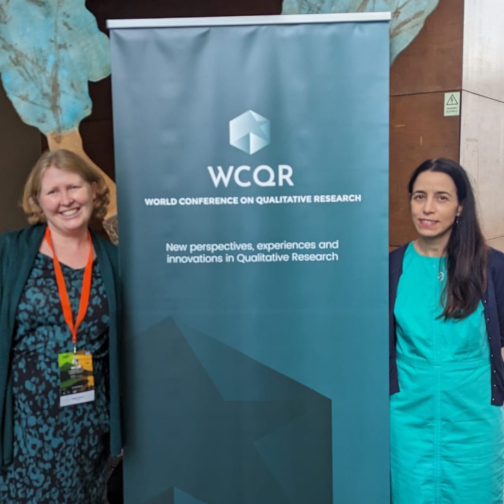 Two women standing on two sides of a  sign board of WCQR, at the University of the Azores for the WCQR.