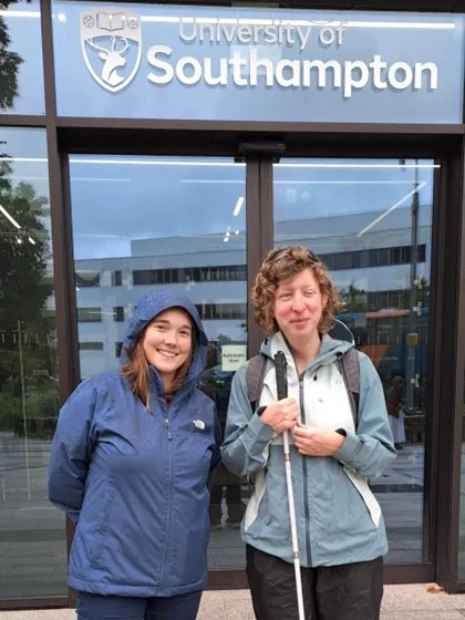 Two women standing in front of a glass door with University of Southampton written on top of the door. The women on the right has a walking stick in her hand.