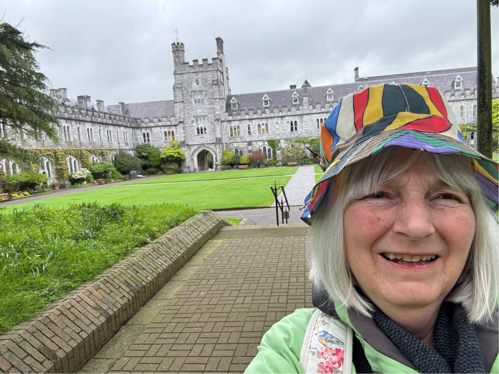 A person with a colourful hat outside a large building and a green lawn. 